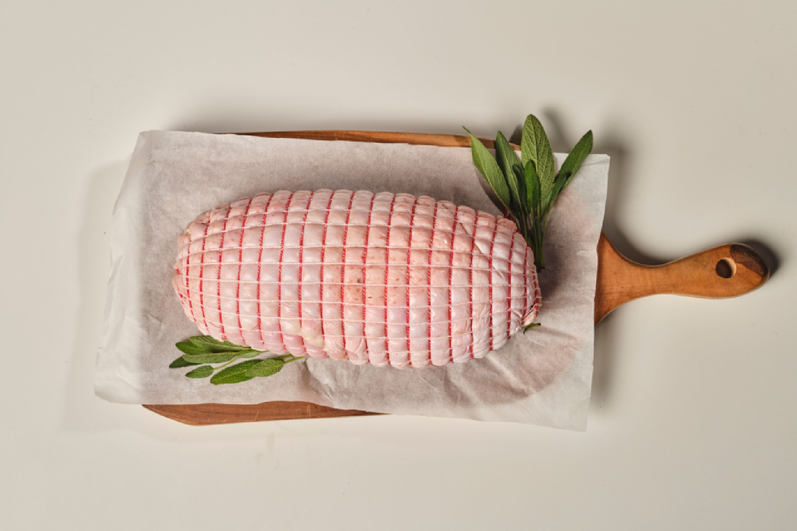 Boned and rolled turkey buff roast with golden skin and fresh herbs served on a carving board.